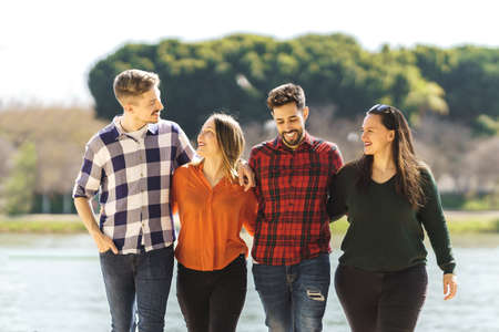 group of friends laughing while strolling near a riverの写真素材