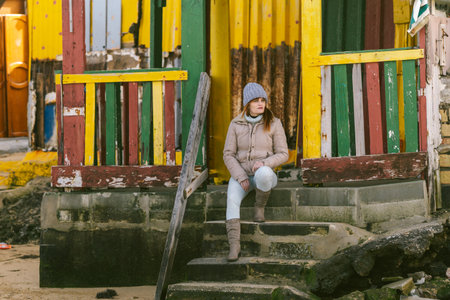 woman in winter clothes sitting on the steps of a colorful house near to the seaの写真素材