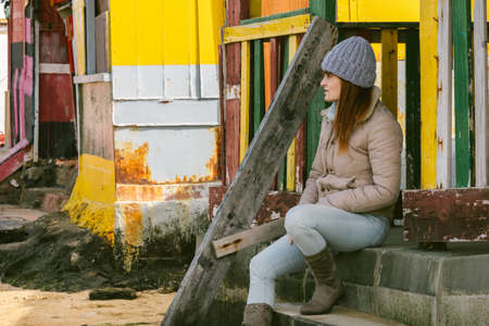 red-haired woman with wool cap sitting on the steps of a house near the seaの写真素材