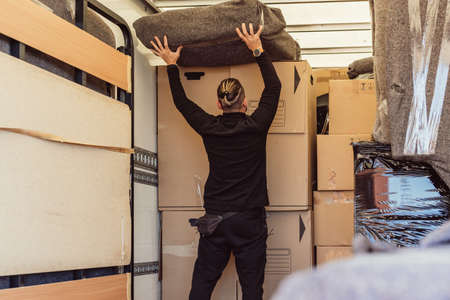 worker with ponytail placing a bundle on top of cardboard boxes inside a moving truckの写真素材