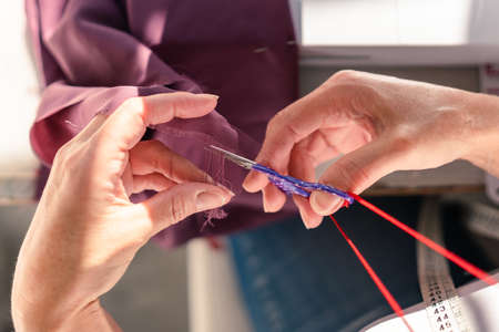 aerial view of hands cutting threads from a piece of fabric with scissorsの写真素材