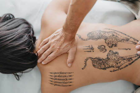 zenith view of a masseurs hand pressing on a womans tattooed upper back.の写真素材