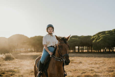 backlit photo of a young rider riding a horseの写真素材