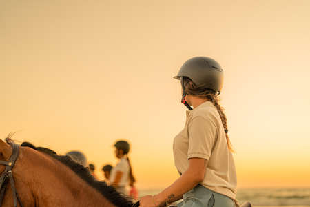 young woman with braid riding on horseback observing her companionsの写真素材