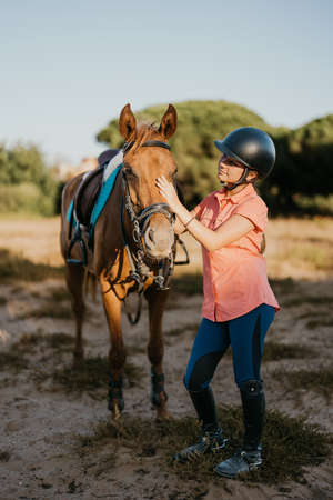 vertical portrait of girl rider standing next to her pony caressing his headの写真素材