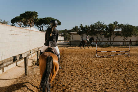rear view of a woman in equestrian attire warming up a horse by circling the equestrian arena.の写真素材
