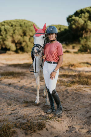 vertical portrait of teenage girl standing in pink dress with her white horseの写真素材