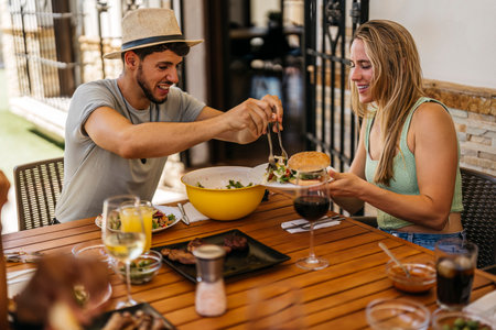 latino man in sombrero tosses some salad as a hamburger to a blonde Caucasian woman