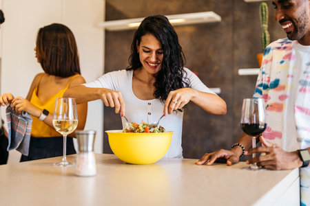 young Latin girl stirring salad next to Latin guy in the kitchenの写真素材