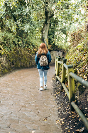 woman walking on a cobblestone road wearing a raincoat and a backpack.