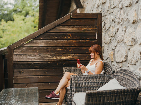 woman with her mobile phone sitting on a hotel room terraceの写真素材