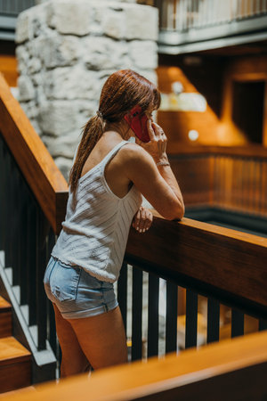 vertical photo of a woman talking on her cell phone on the wooden stairs of a hotelの写真素材