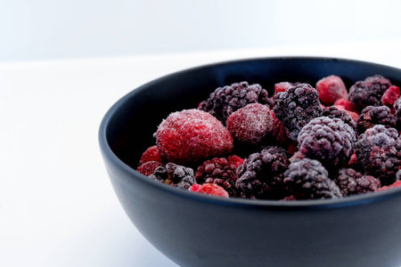 Frozen Berries in black bowl on white surfaceの写真素材