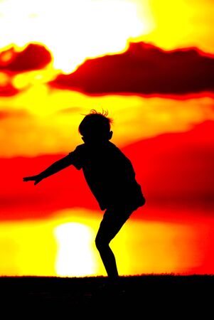 Silhouette of a boy  on orange sunset background.の写真素材
