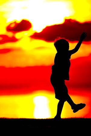 Silhouette of a boy  on orange sunset background.の写真素材