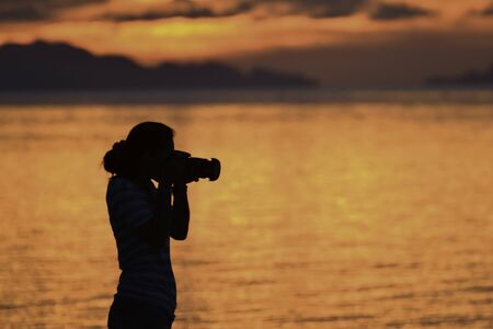 Silhouette of woman photographer during sunset on the beach.