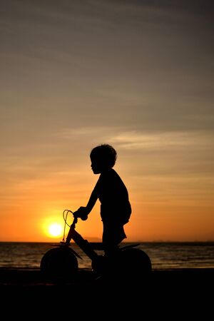 silhouette of small boy on bike at dusk.の写真素材