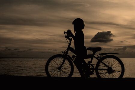 silhouette of small boy on bike at dusk.の写真素材