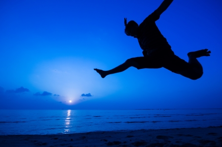 silhouette of happy man jumping at the beach.の写真素材