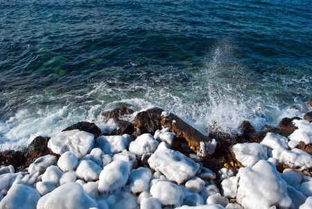 Stones under snow and ice on seacoastの写真素材