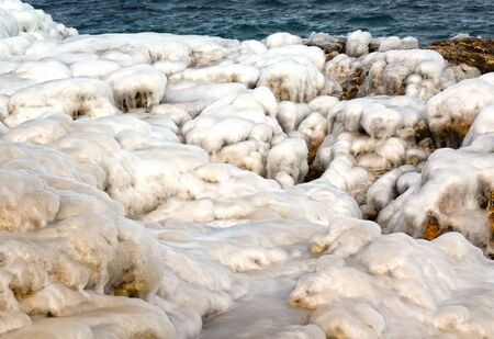 Stones under snow and ice on seacoastの写真素材