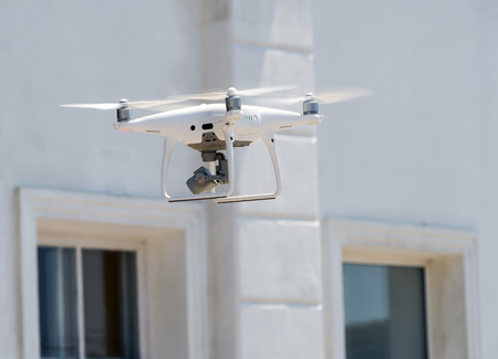 Flying drone quadcopter in front of white building
