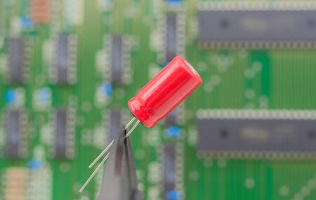 Electronic component held with tweezers over a green motherboard