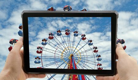 Close up hand holding black smartphone and photographs Ferris wheel