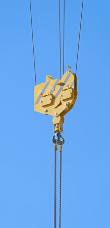 Crane hook hanging on steel ropes on background of blue sky