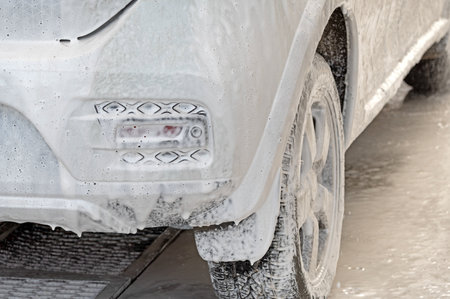 white car in soap foam on the car washの写真素材