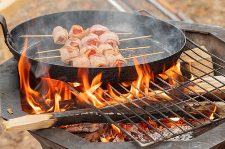 A cast-iron frying pan with meat stands over a fire on a metal gate