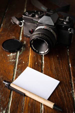 blank notebook with a ballpoint pen and old vintage photo camera on wooden backgroundの写真素材