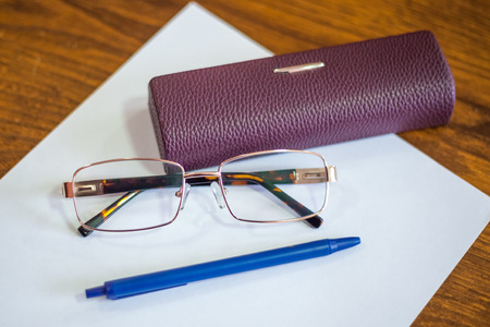ballpoint pen on a sheet and reading glasses with box.