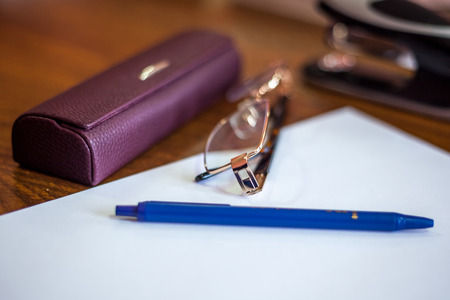 ballpoint pen on a sheet and reading glasses with box.