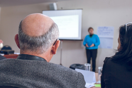 Speaker giving presentation in lecture hall. Participants listening to lecture and making notes.の写真素材
