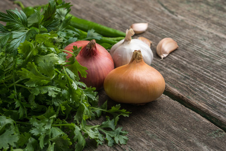 Onion, corn, garlic, pepper, coriander and parsley on an old wooden board.の写真素材