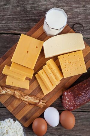 cheese and dairy products on a wooden board with eggs and sausage.