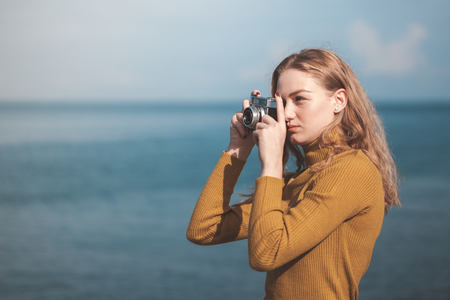 beautiful blonde girl on a sea beach with a old camera in hand.の写真素材