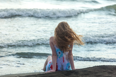 Beautiful girl sits on a sandy beach on the seashore.の写真素材