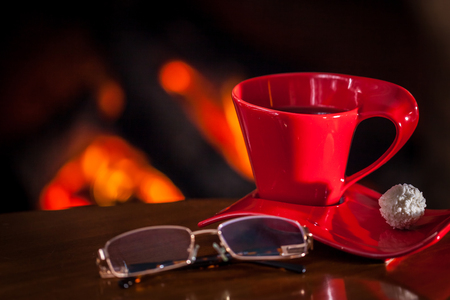 Red cup of tea or coffee and chocolate near fireplace on wooden table. Winter and Christmas holiday concept.の写真素材