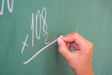 schoolgirl with chalk at the blackboard solves a math problem.
