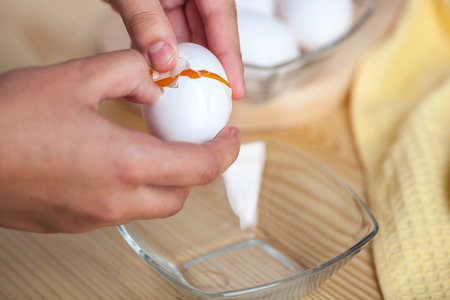Woman hands breaking an egg to separate egg white and yolks, egg shells at the background.の写真素材