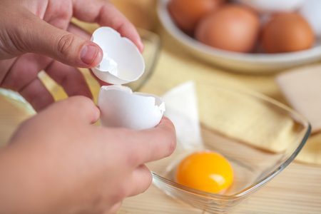 Woman hands breaking an egg to separate egg white and yolks, egg shells at the background.の写真素材