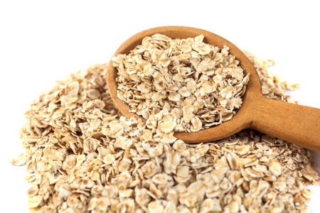 Heap of rolled oats with wooden spoon on white.