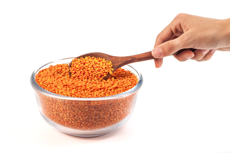 Yellow lentil in glass bowl with wooden spoon in the hand isolated on white background.の写真素材