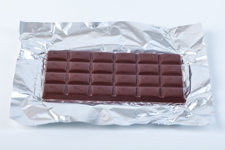 Dark chocolate bar in opened silver foil. Sweet food.