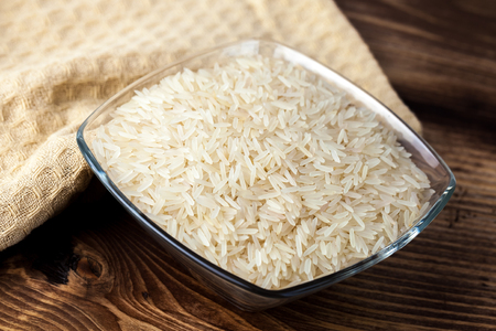 Seeds of white rice in glass bowl on wooden table, ingredient for cooking.の写真素材