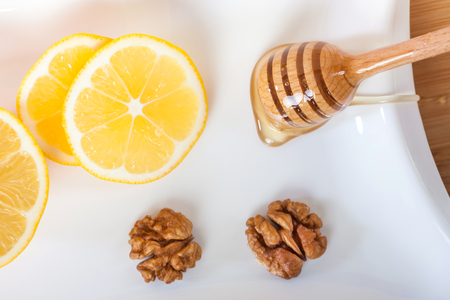 honey in a white ceramic bowl with honey dipper and lemon on a wooden kitchen board.の写真素材