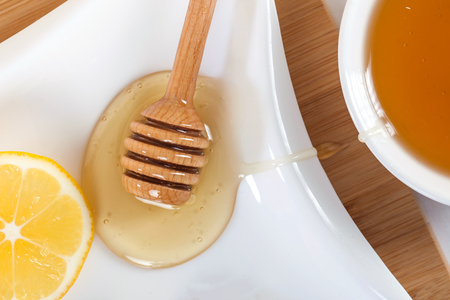 honey in a white ceramic bowl with honey dipper and lemon on a wooden kitchen board.の写真素材