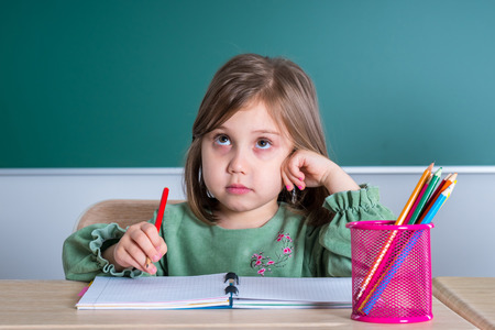 Little pretty girl sitting in the classroom at the gray desk and draws.の写真素材